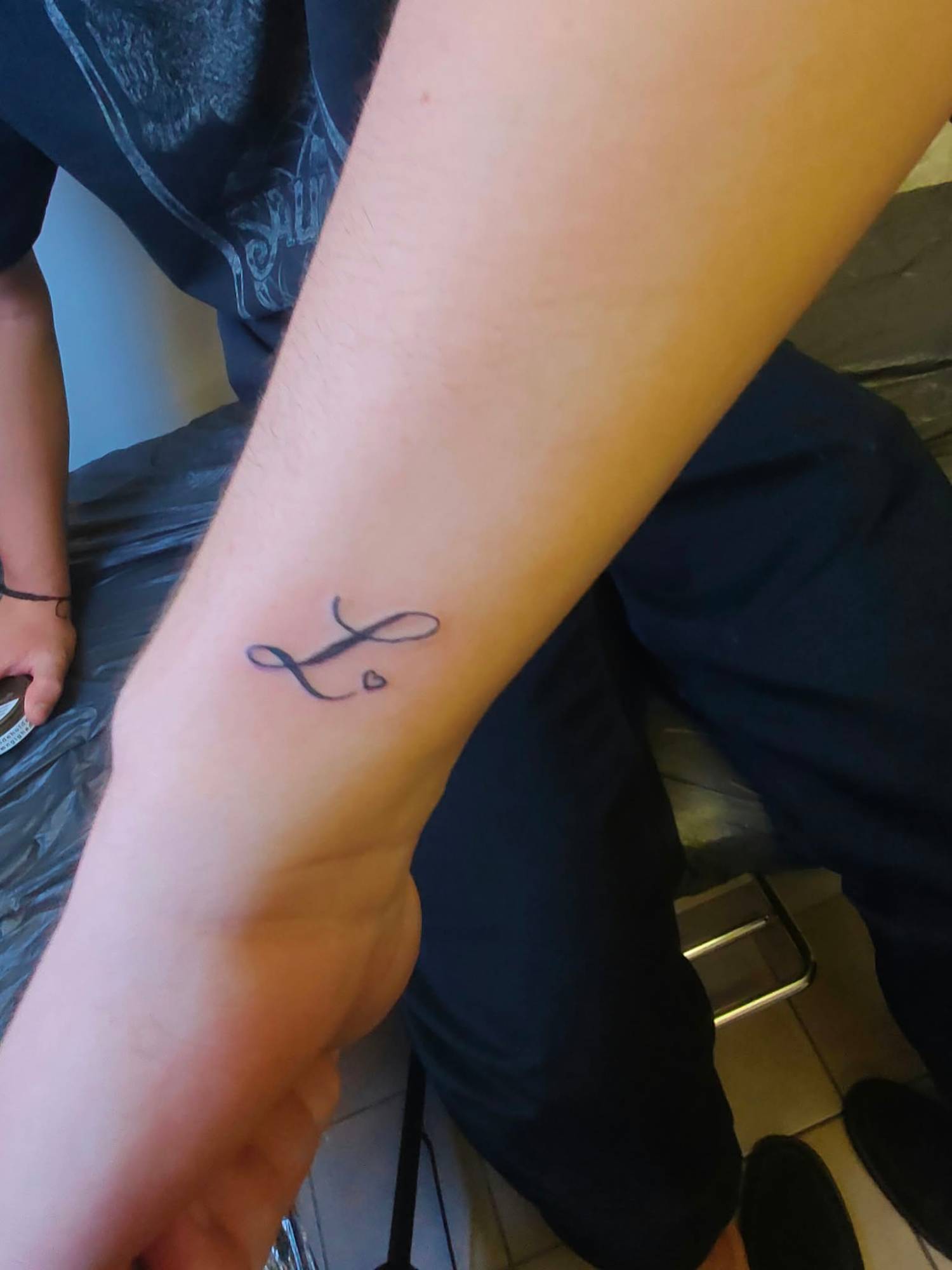 Initial L med sløjfe og lille hjerte, fin streg, underarm.
